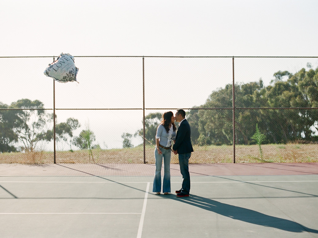 copule pose on tennis court with love balloon on string during la jolla elopement photo shoot
