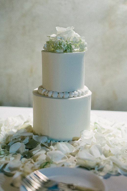 simple two tier wedding cake surrounded by white rose petals