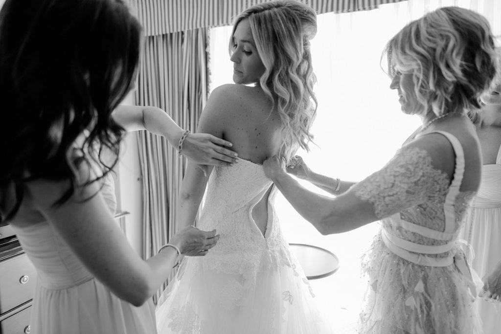 mother and bridesmaid help bride put on gown
