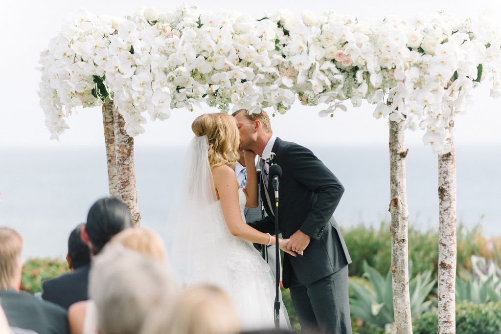 bride and groom kissing under flower arch montage laguna beach wedding