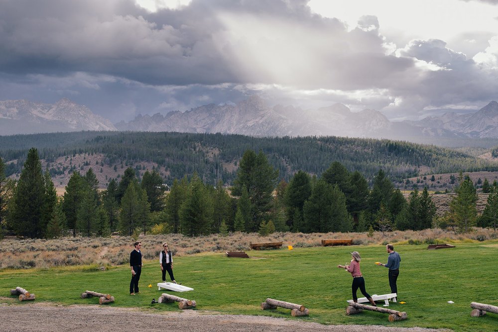 four guests play cornhole on lawn overlooking sawtooth mountains at idaho rocky mountain ranch destination wedding