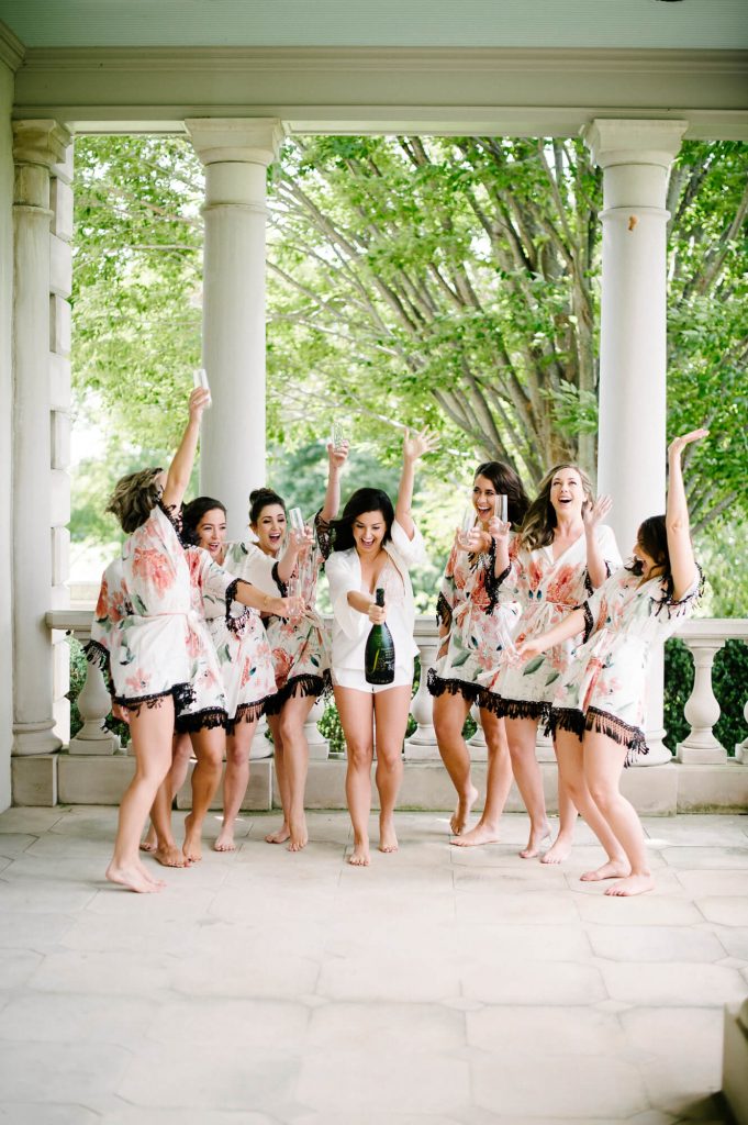 bride and bridesmaids in matching robes pop champagne during great marsh estate wedding