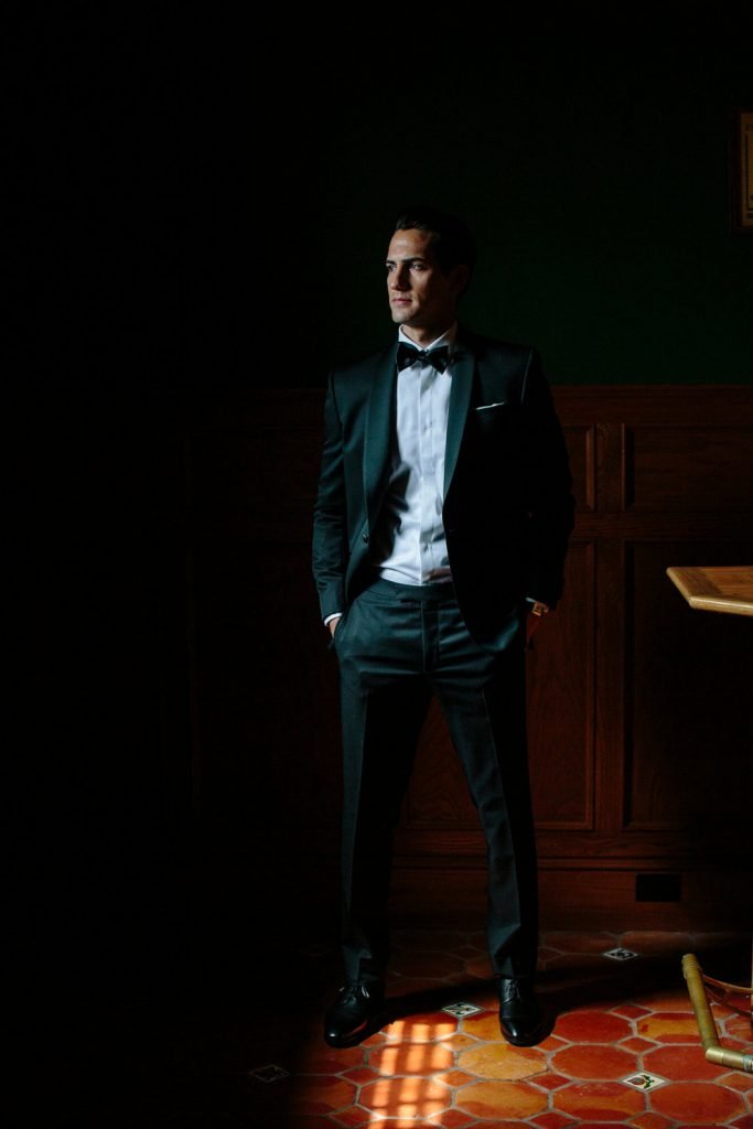 portrait of groom in traditional tuxedo in wood paneled bar