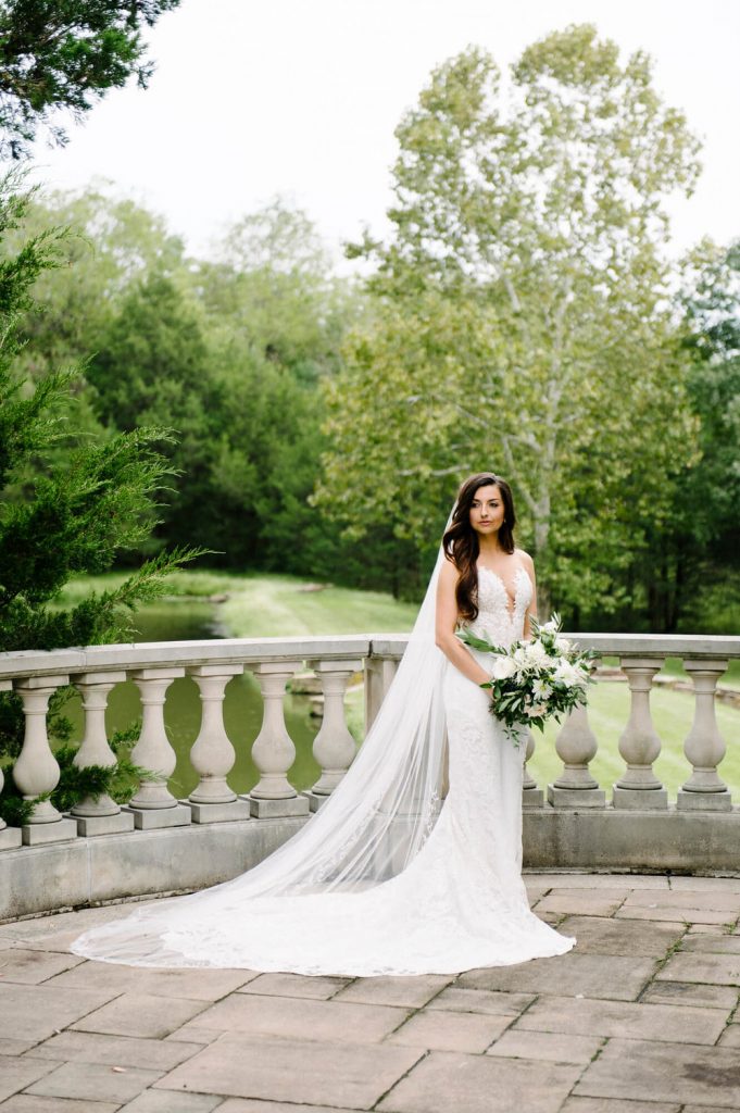 bridal portrait in long train and veil with flowers on stone railing at great marsh estate