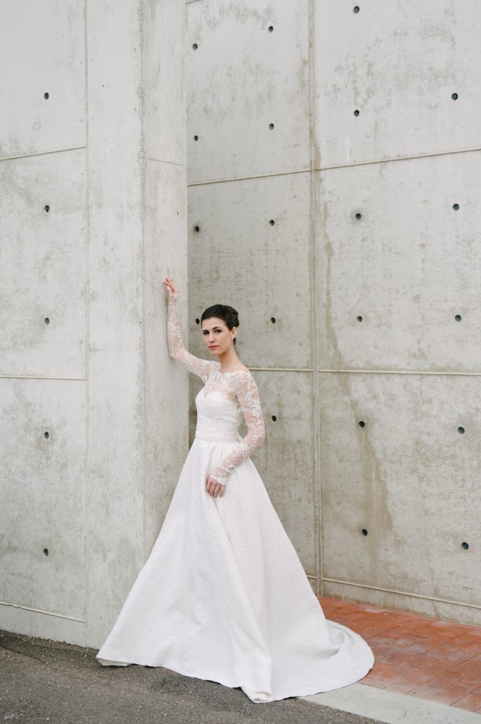 bride in gown with long train and lace sleeves poses at salk institute la jolla bridal portrait
