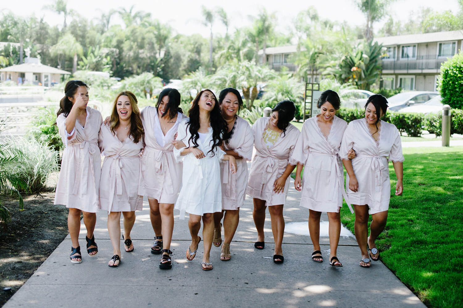 bride and bridesmaids laugh and walk in matching pink robes at the dana mission bay