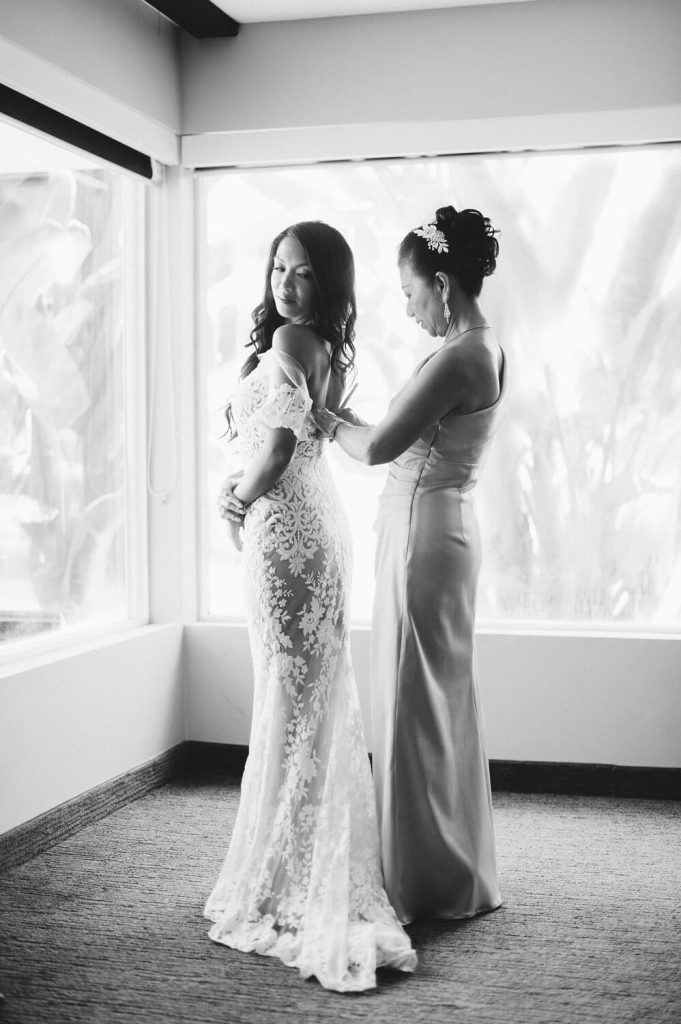 bride's mother helps daughter into lace wedding gown at dana mission bay