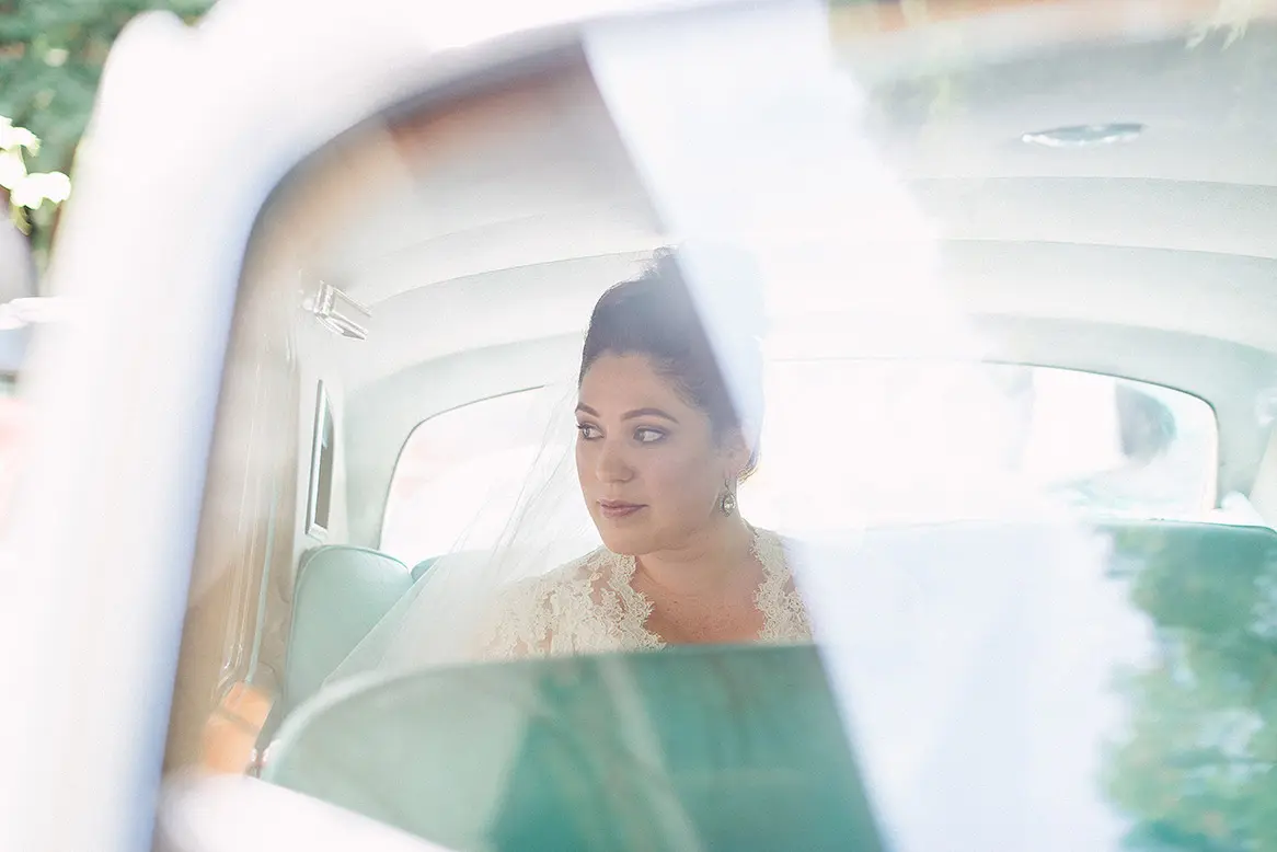 bride waits outside church in vintage white rolls royce limousine with teal interior