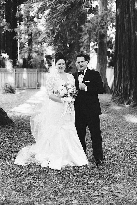 bride and groom pose amongst trees outside our lady of wayside church