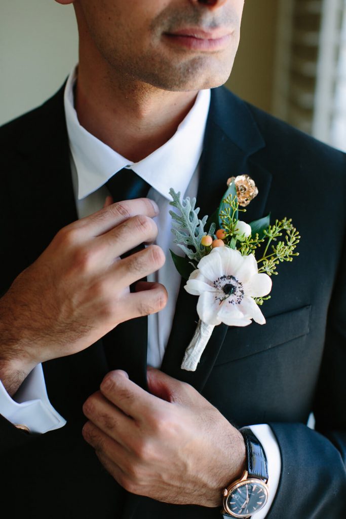 groom tightens tie with boutonniere and rose lapel pin 