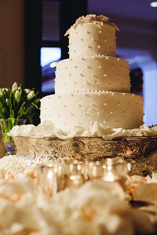 elegant three tier wedding cake surrounded by white rose petals with candles on table