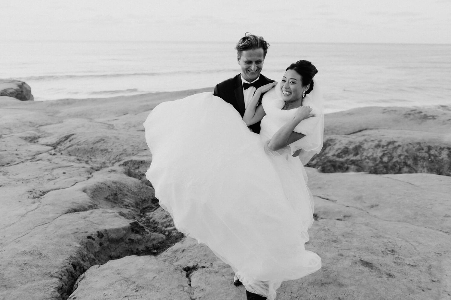 groom carries bride ocean beach