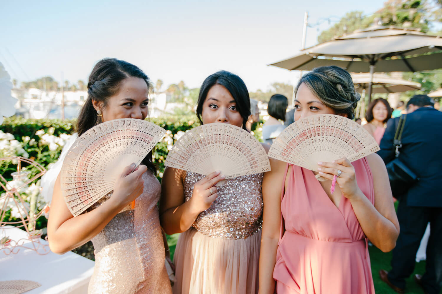 bridesmaids smile at camera covering faces with custom hand fans as wedding favor