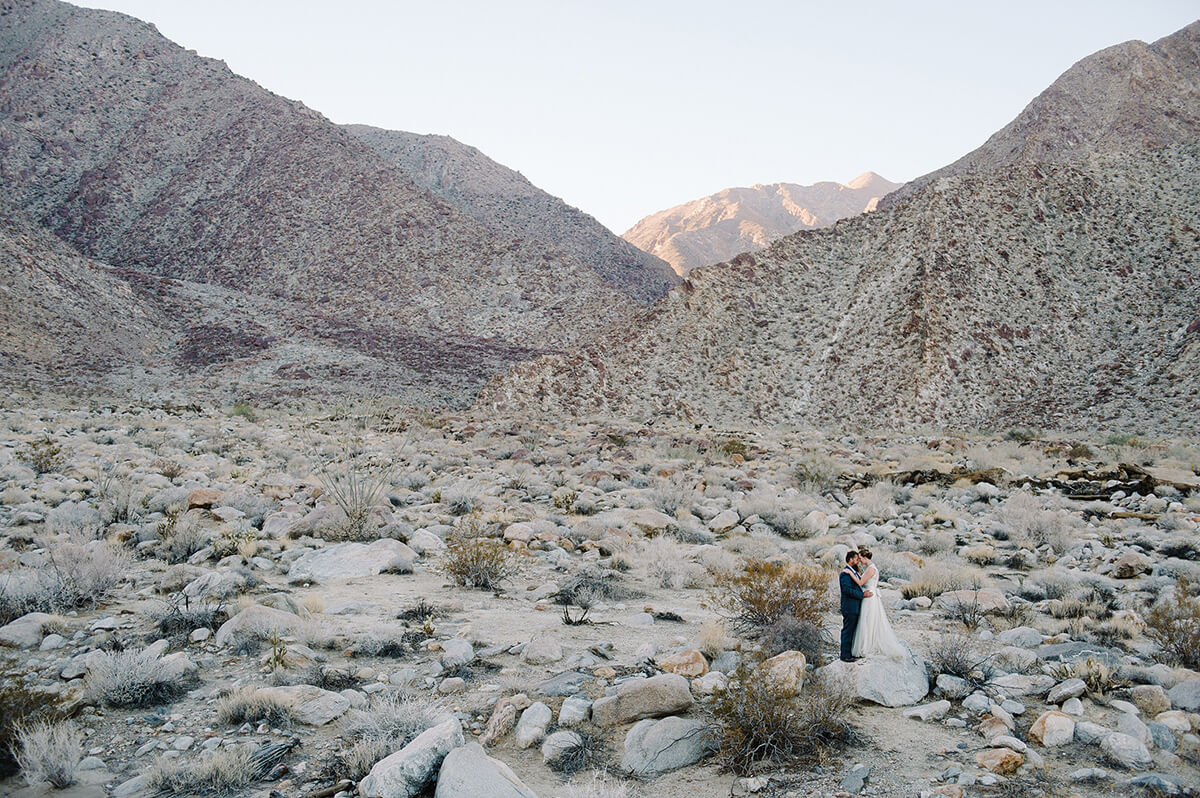 bride and groom pose on rock at base of large desert canyon in borrego springs