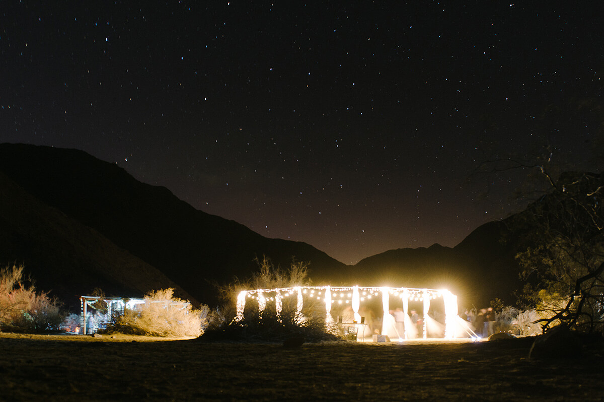 circle of poles draped in white thule hold market lights and illuminate the night sky at desert wedding reception in borrego springs