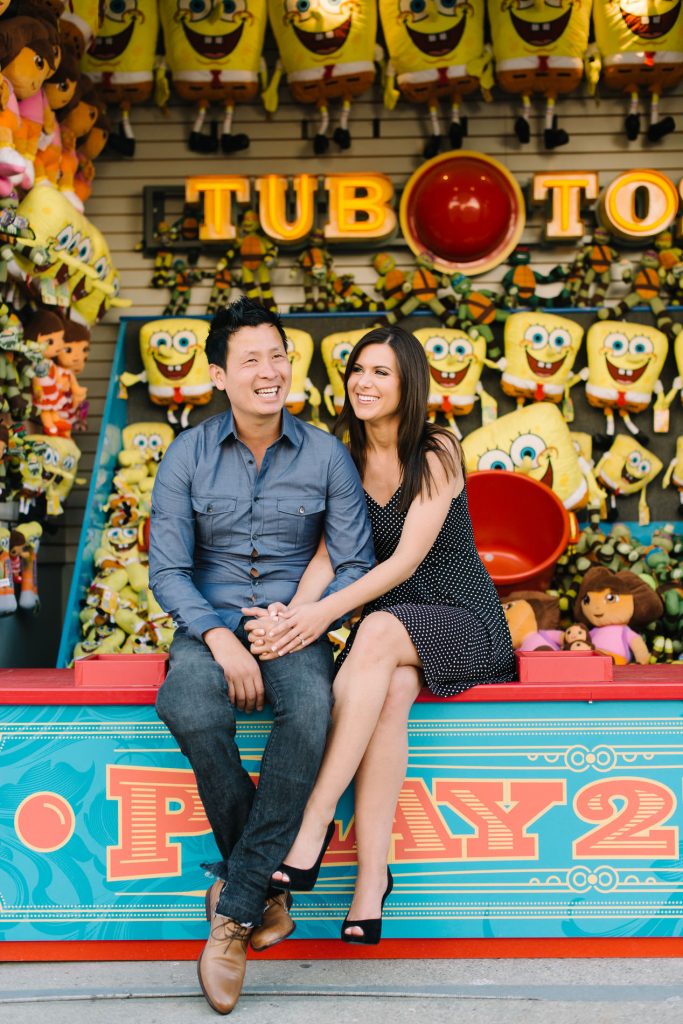 couple posing on tub toss game belmont park engagement photos