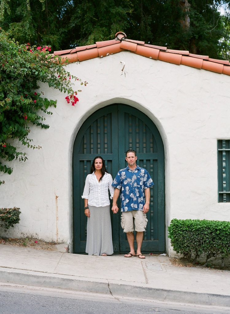 couple holding hands in front of green door and arch in avalon for catalina island engagement photos