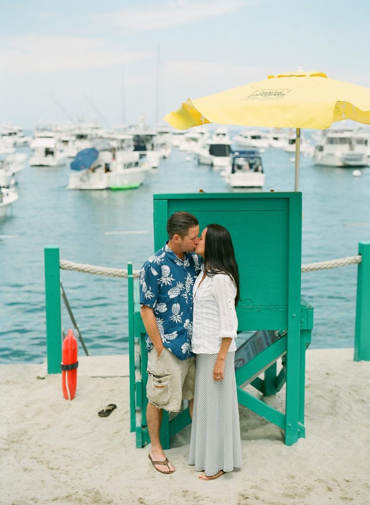 couple kissing in front of large green lifeguard chair on beach in avalon for catalina island engagement photo