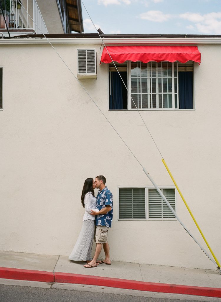 couple kissing on wall with red awning over window downtown avalon catalina island engagement photos
