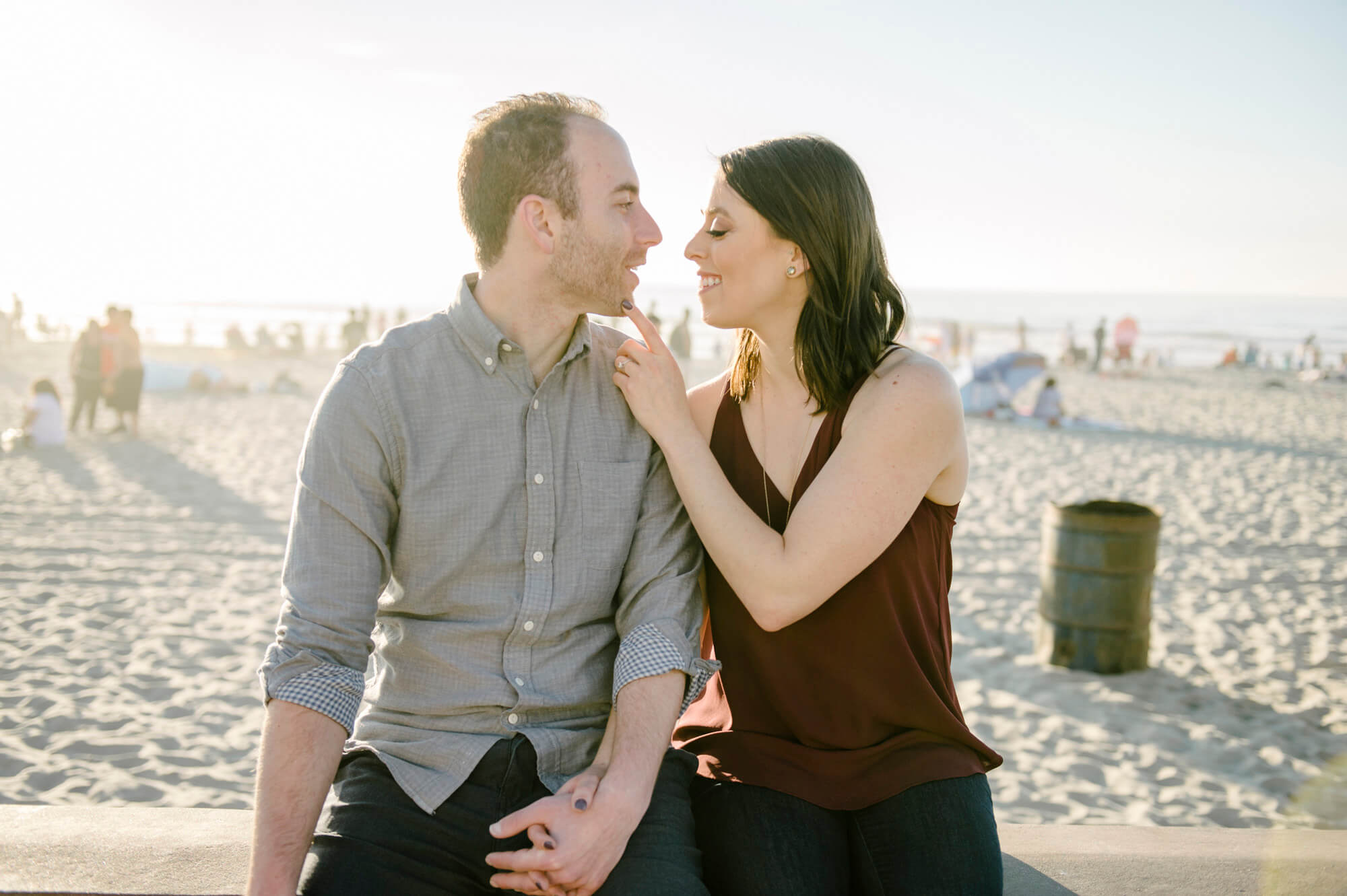 couple sit on wall at boardwalk for mission beach engagement photo