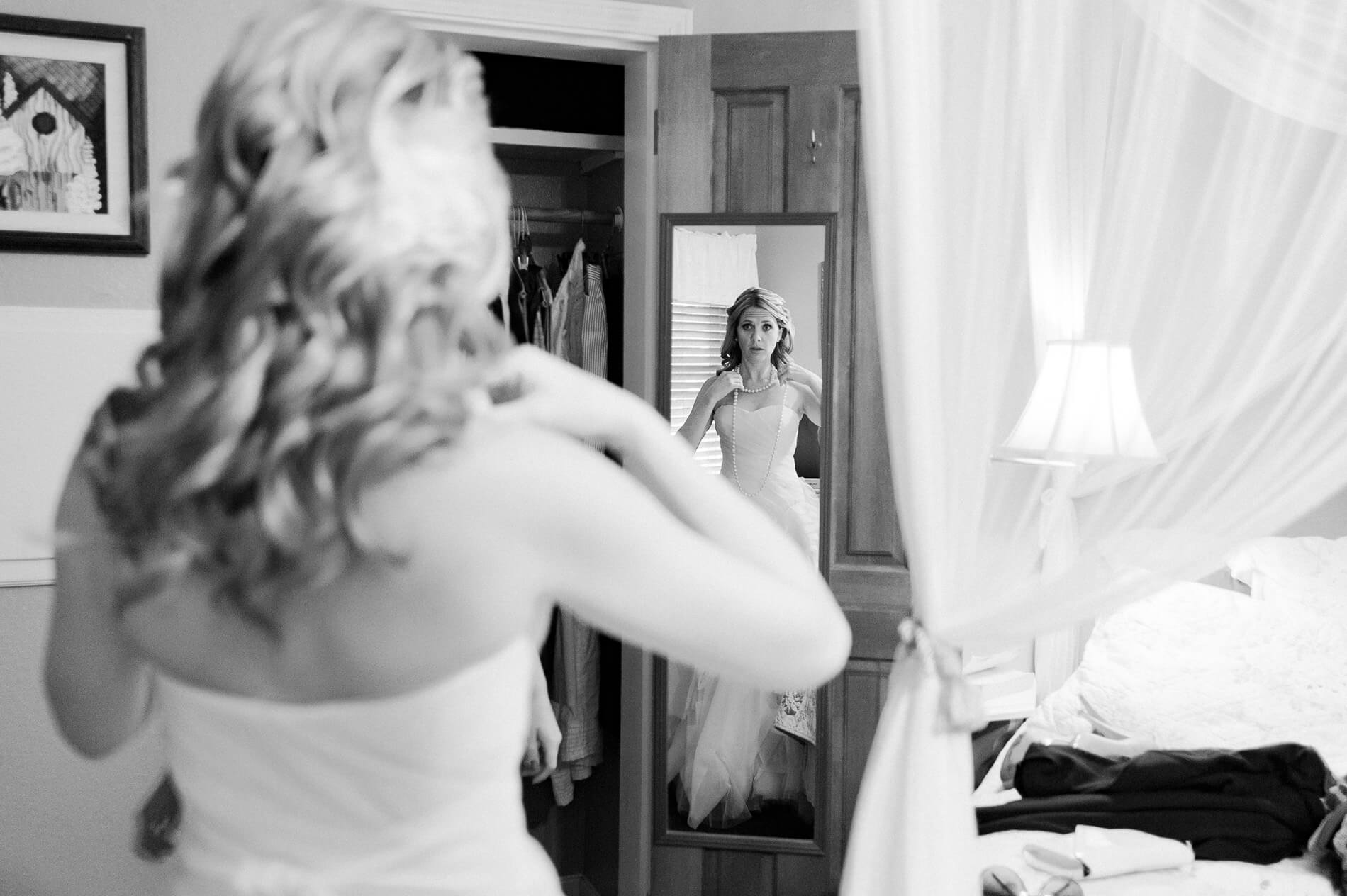 bride adjusting long necklace in mirror