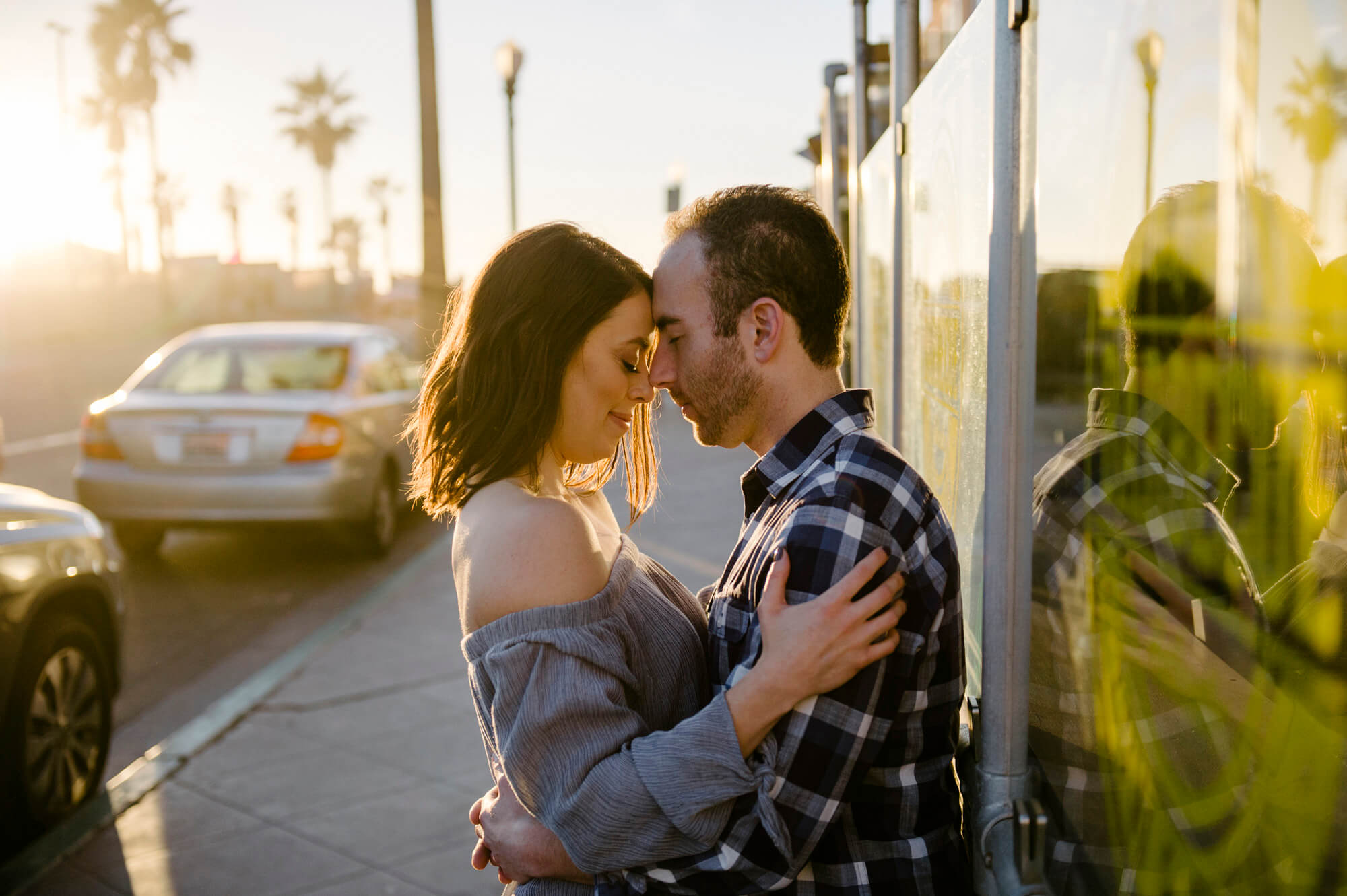 engaged couple embrace against restaurant window in mission beach as sun sets