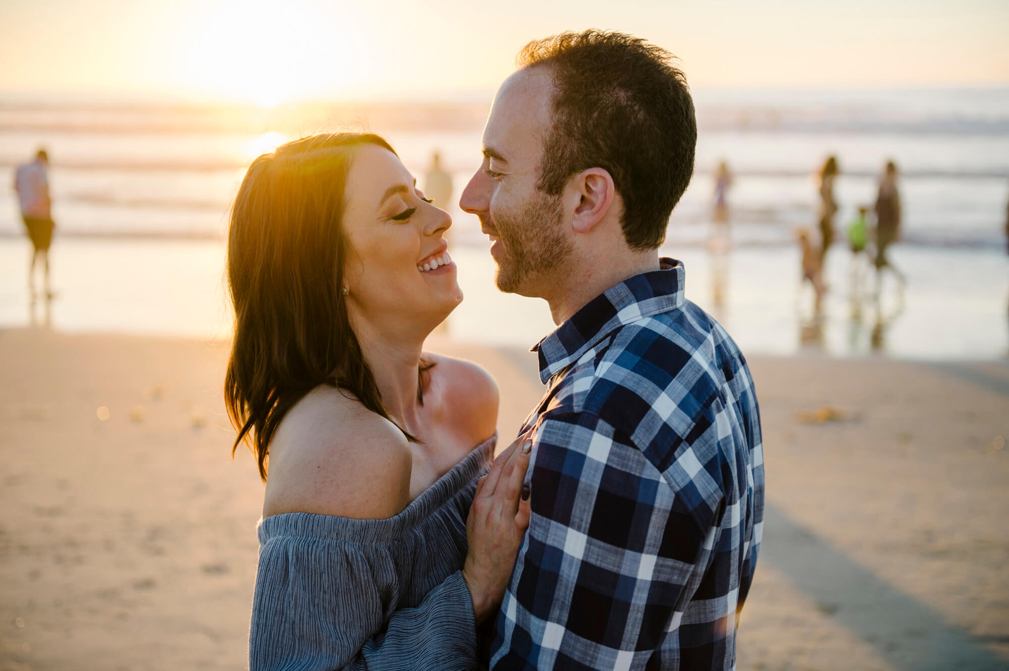 engaged couple laugh on mission beach at sunset