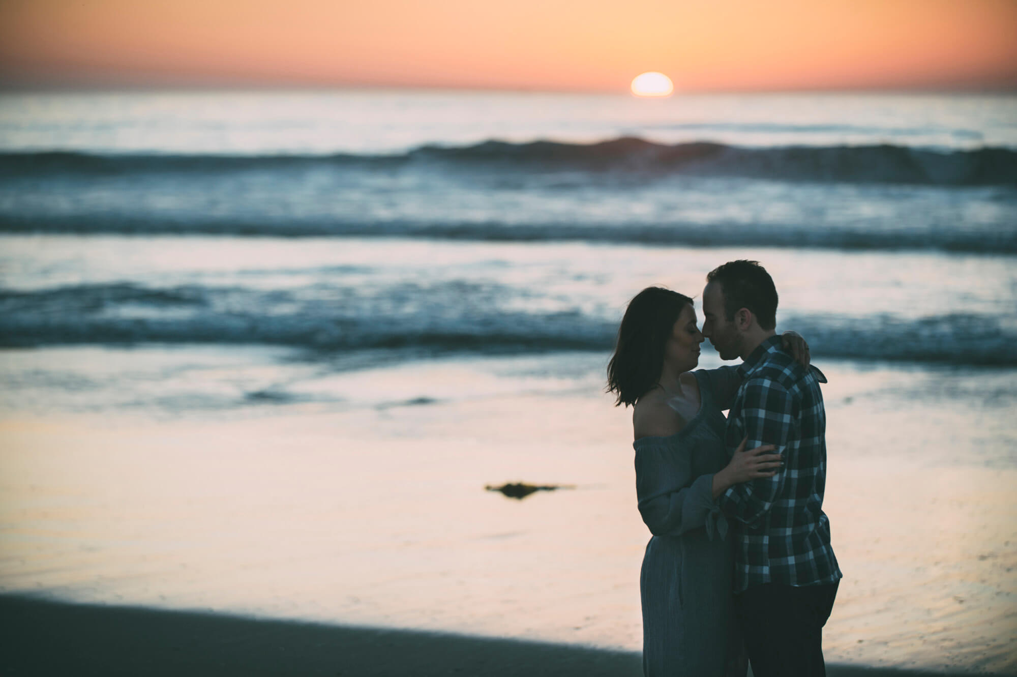 engaged couple kiss on beach at sunset