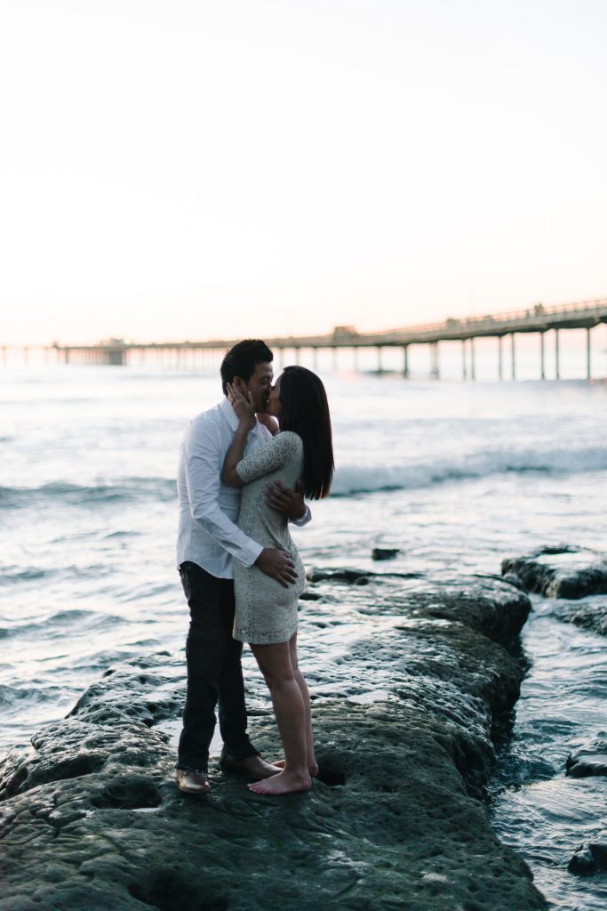 couple kissing on rocks near ob pier engagement photo