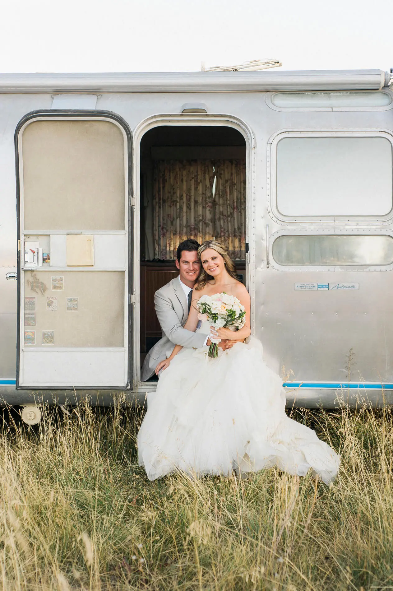 couple sitting in doorway of vintage airstream rustic barn wedding