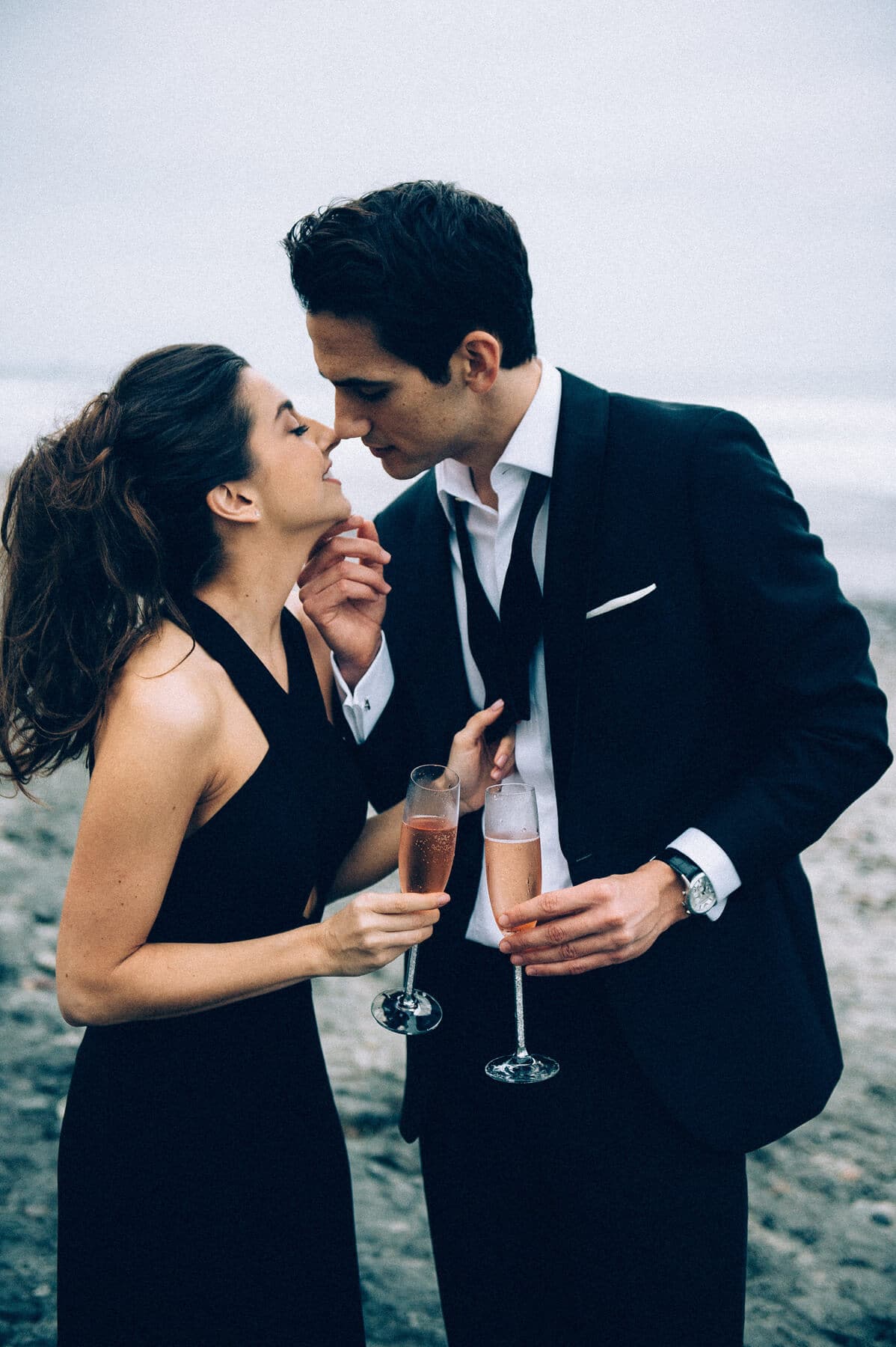 couple holding glasses of sparkling rose kissing torrey pines engagement photo