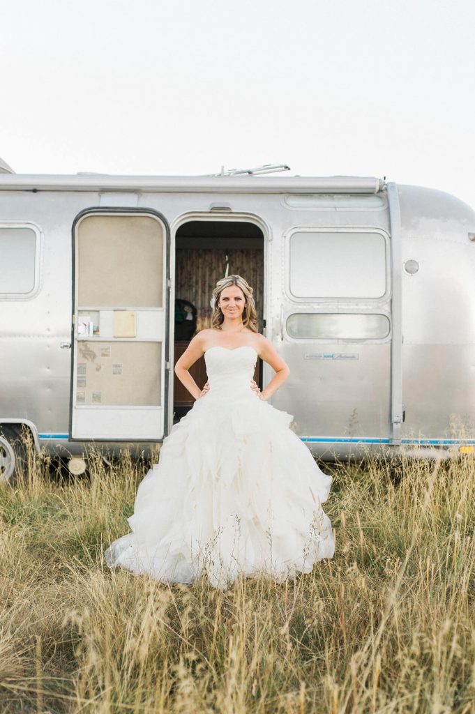 bride wearing strapless vera wang gown posing in front of vintage airstream trailer rustic barn wedding lake almanor