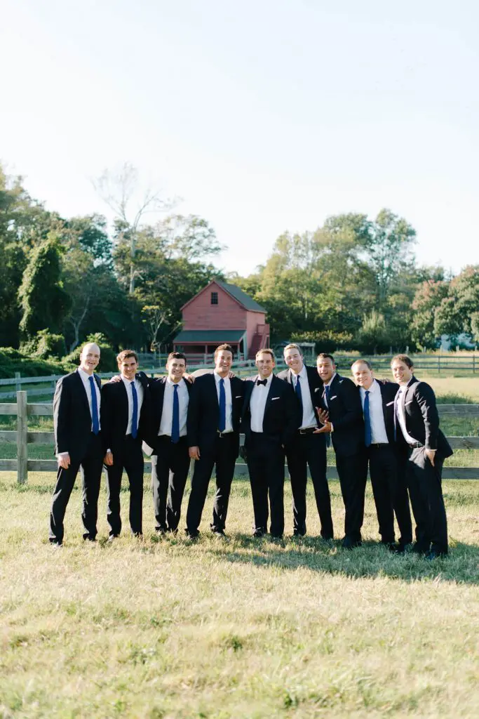 groom and groomsmen posing in field near old red barn cape may new jersey