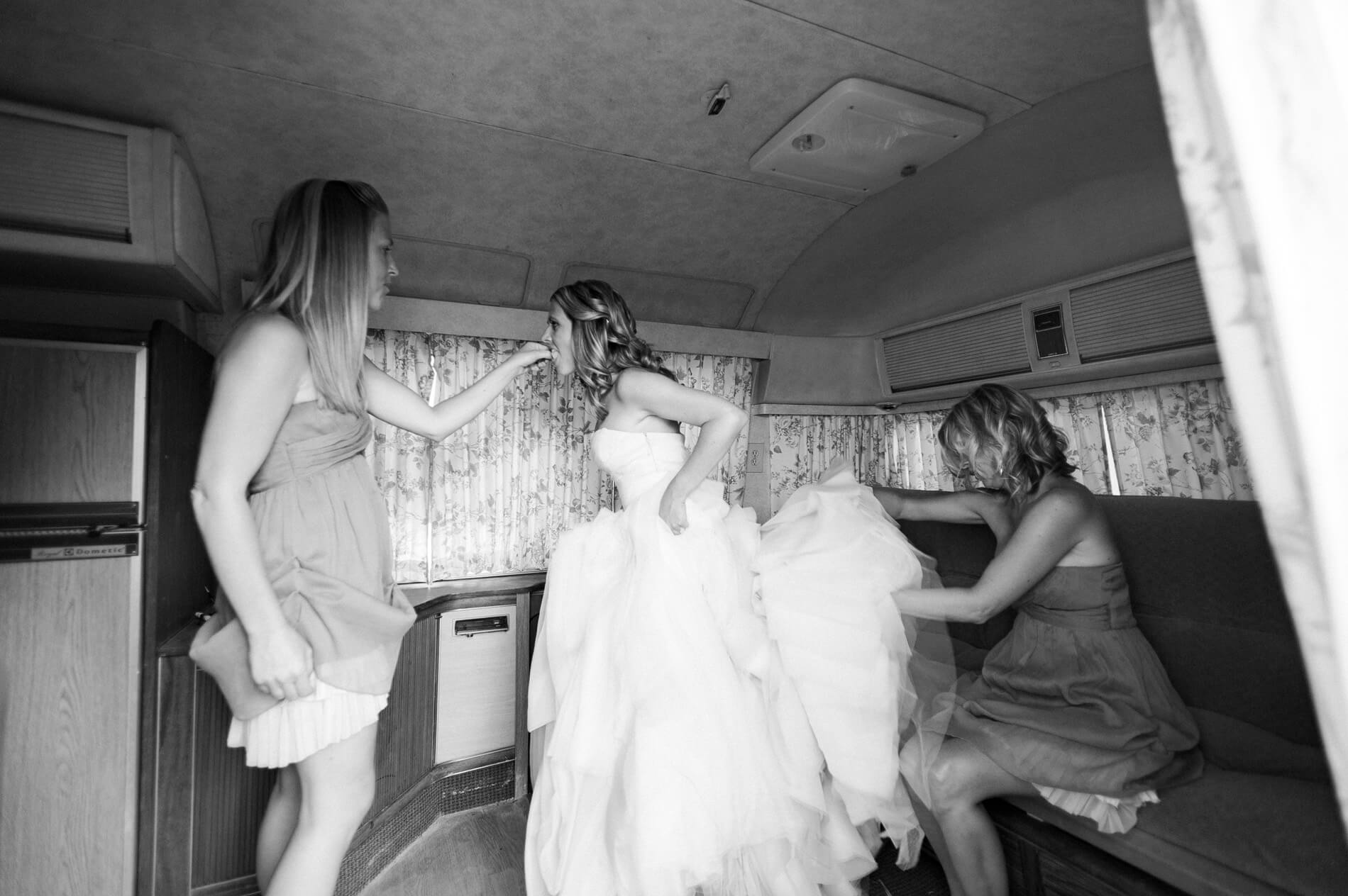 bridesmaids feeding bride and helping bustle inside vintage airstream trailer