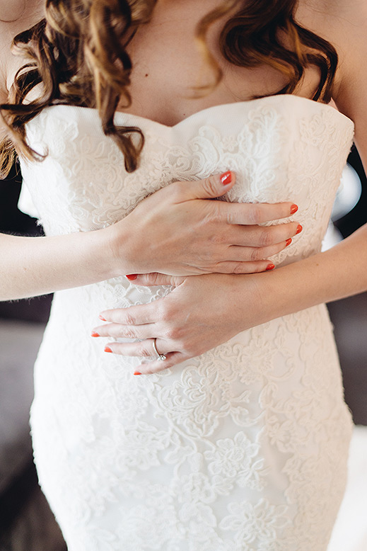 bride's hands rest across chest while gown is being put on