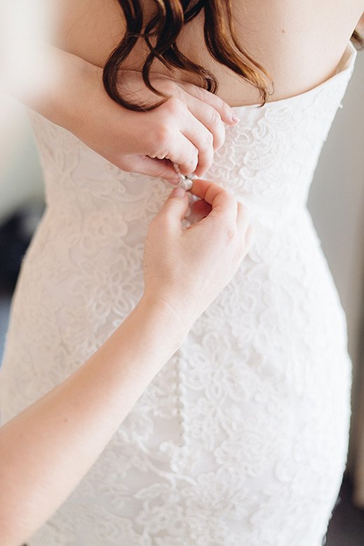 hands buttoning up back of wedding gown