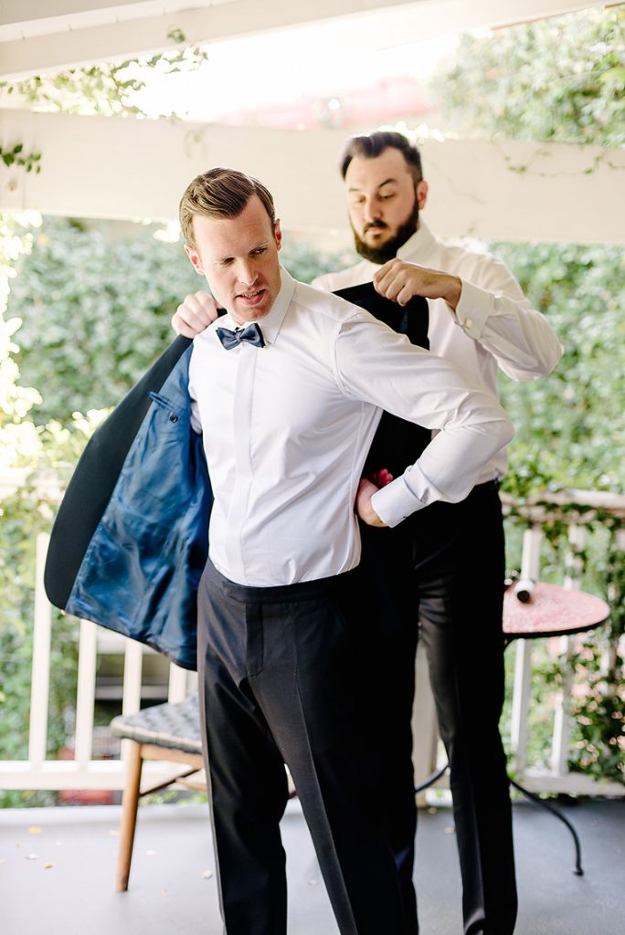 groomsman helps groom into tuxedo jacket