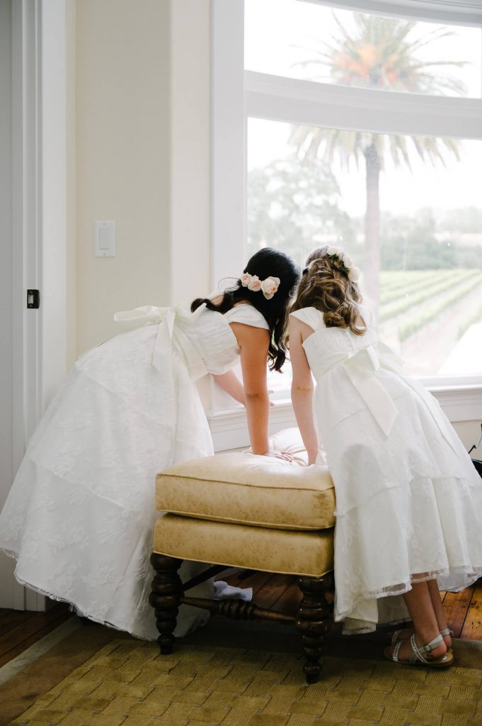 two flower girls looking out window for arriving guests at crossroads estate