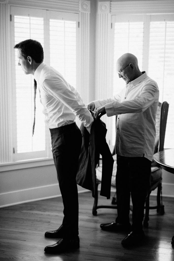 grooms father helping son with suit jacket before wedding
