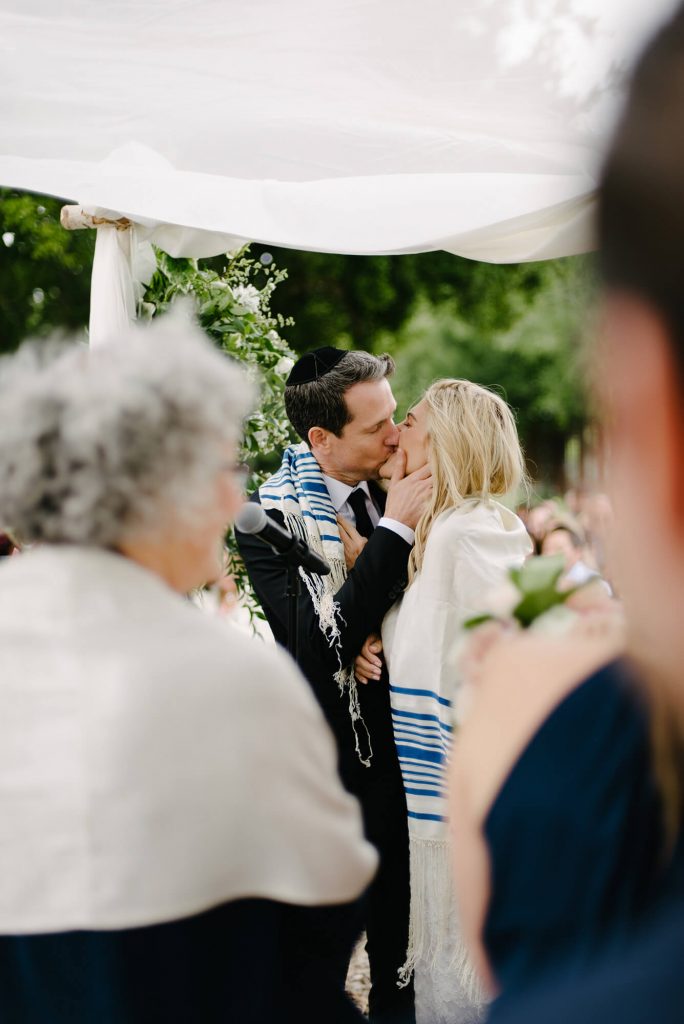 bride and groom wrapped in jewish garment kiss during crossroads estate wedding