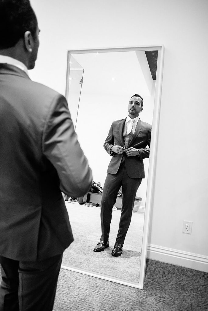 groom buttoning suit jacket in mirror