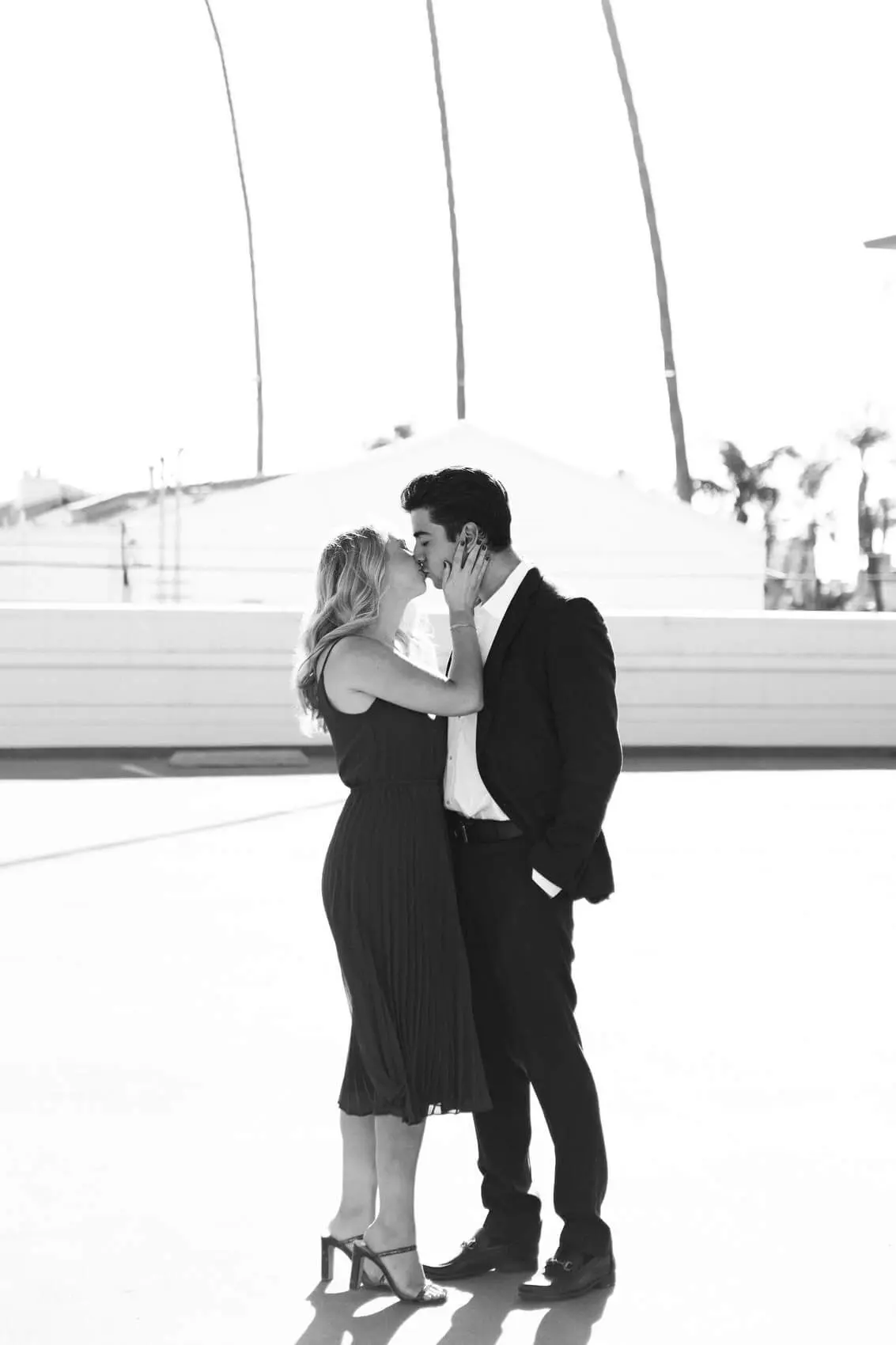 woman in long dress and man in dark suit kiss on rooftop in downtown la jolla romantic engagement photo