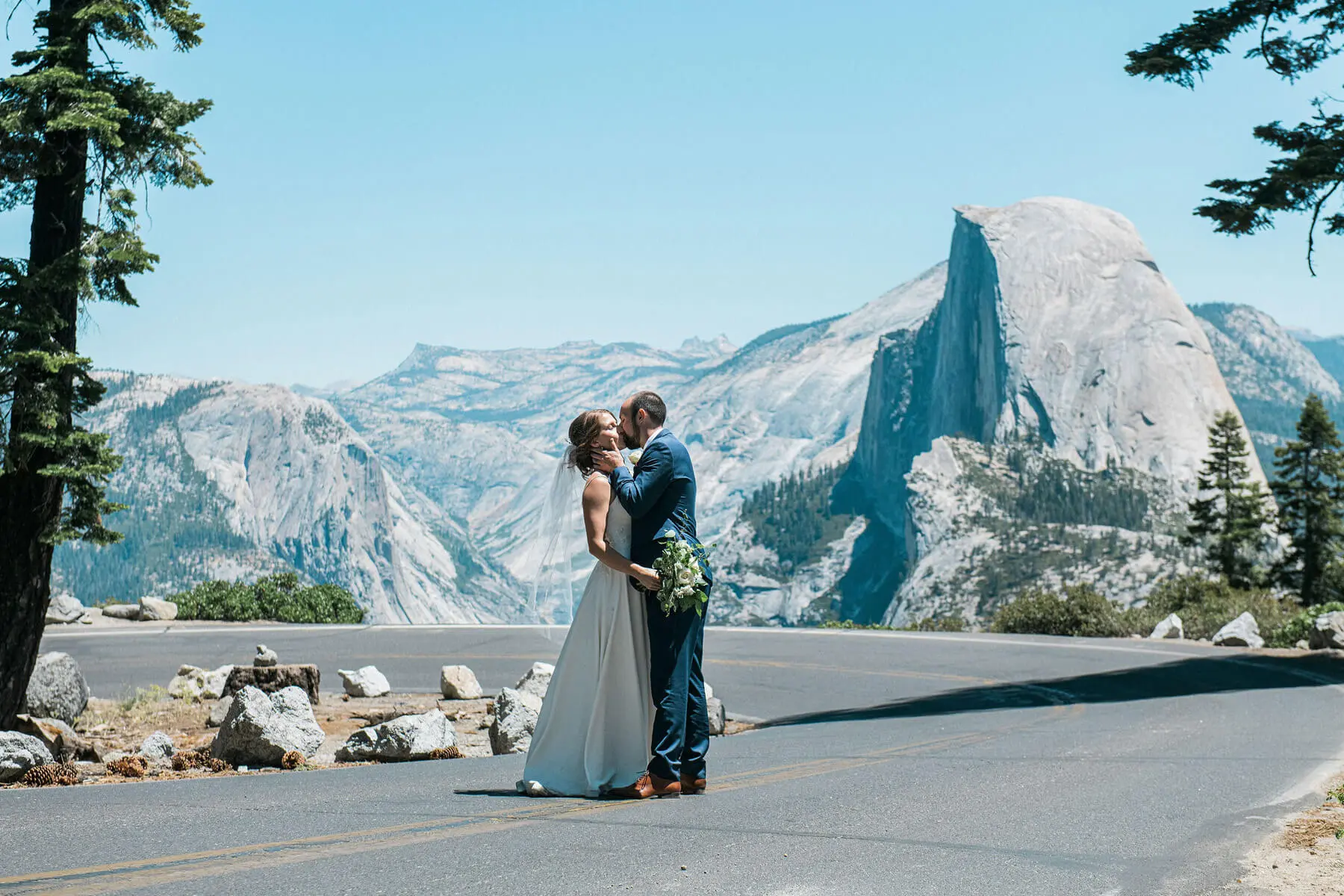 bride and groom kissing on road to glacier point with halfdome in background yosemite adventure elopement