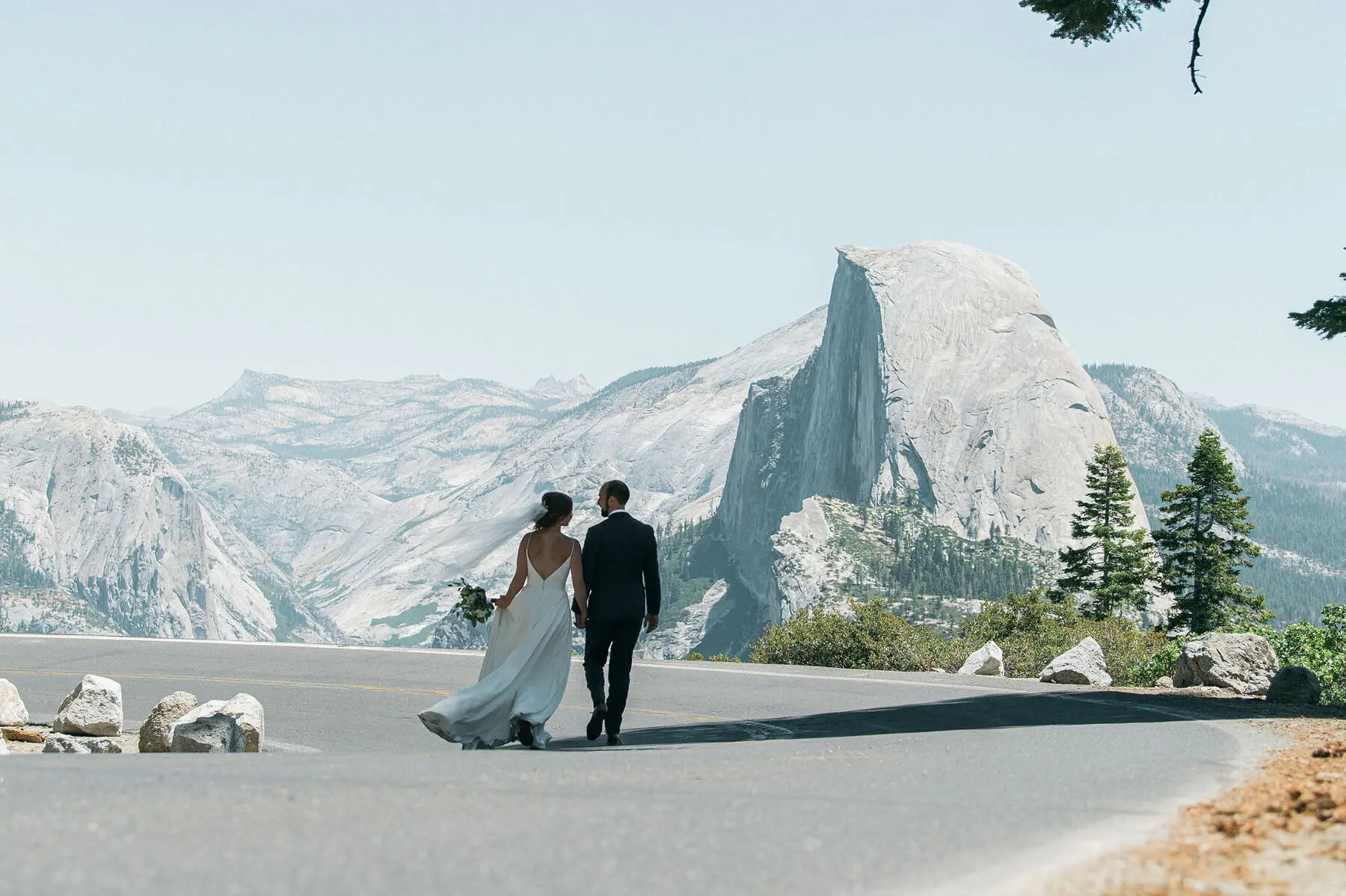bride and groom walking on road to glacier point with halfdome in background yosemite adventure elopement