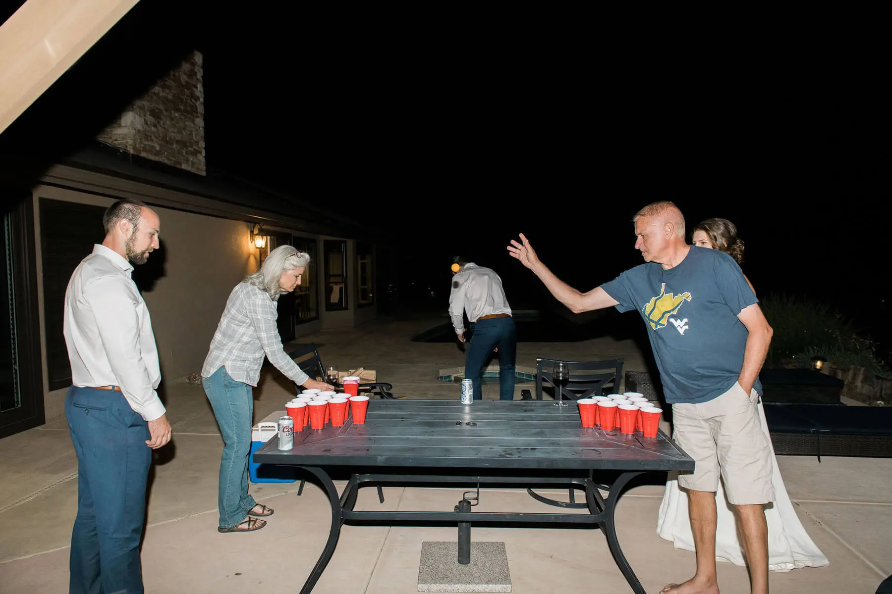 bride and groom and family play beer pong on patio of private residence during intimate wedding reception oakhurst